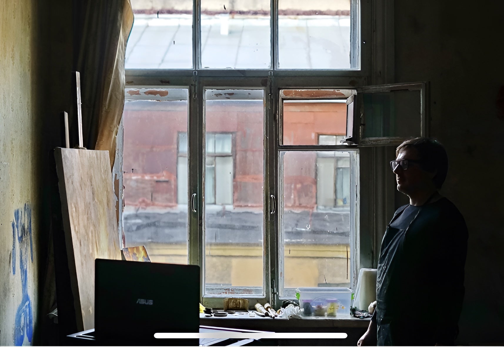 Denis Ichitovkin in his studio with paintings and a window behind him.